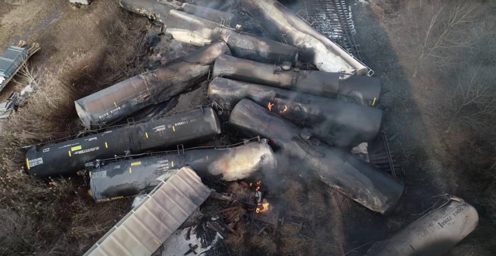 Charred Norfolk-Southern railcars pile up in East Palestine following the derailment and toxic vent and burn.