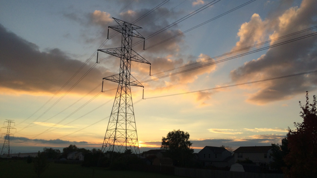 The sun sets behind a transmission tower.